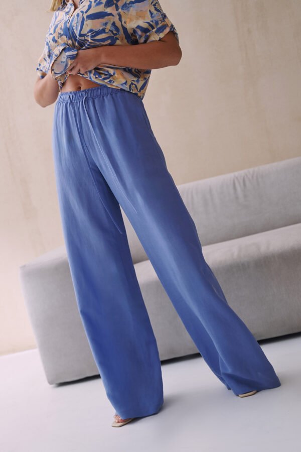 Niebieskie spodnie damskie z wiskozy i lnu z luźnymi nogawkami, wiązaniem w pasie, noszone przez modelkę.