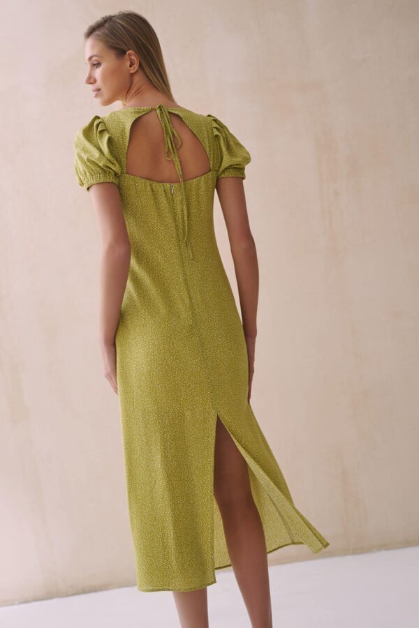 Kobieta w zielonej sukience midi z wzorem w groszki, bufiastymi rękawami i eleganckim rozcięciem z tyłu.