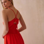 Widok z tyłu kobiety ubranej w czerwoną sukienkę z efektownym wiązaniem na plecach.