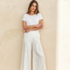 Modelka w białych spodniach culottes z wiązaniem i kieszeniami po bokach, z szeroką nogawką z falującego materiału