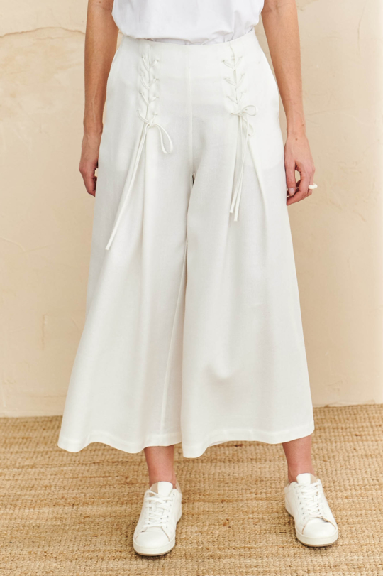 Modelka w białych spodniach culottes z wiązaniem i kieszeniami po bokach, z szeroką nogawką z falującego materiału