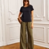 Modelka w khaki spodniach z szerokimi nogawkami i beżowym topie, pozująca w eleganckim wnętrzu