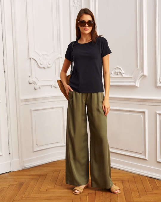 Modelka w khaki spodniach z szerokimi nogawkami i beżowym topie, pozująca w eleganckim wnętrzu