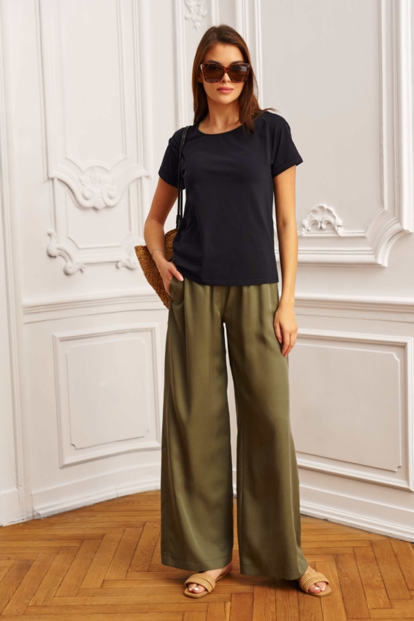 Modelka w khaki spodniach z szerokimi nogawkami i beżowym topie, pozująca w eleganckim wnętrzu