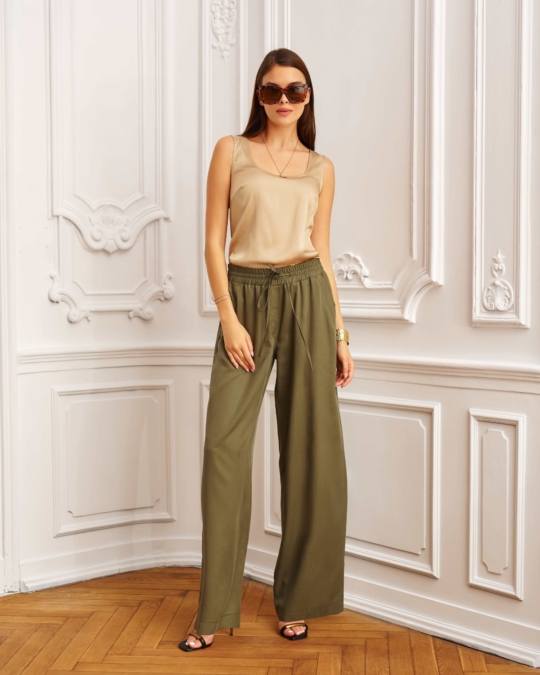 Modelka w khaki spodniach z szerokimi nogawkami i beżowym topie, pozująca w eleganckim wnętrzu