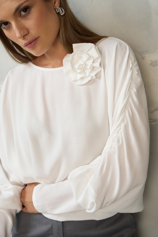 Biała bluzka z ozdobnym kwiatem EZURI w stylizacji z szarymi spodniami