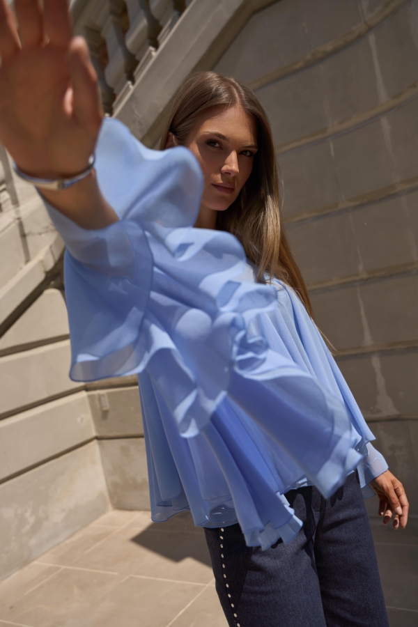 Błękitna bluzka EZURI z szerokimi, falującymi rękawami w ruchu