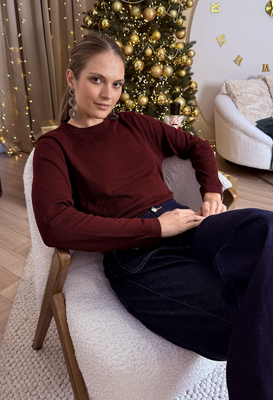 Modelka w bordowym swetrze z miękkiej dzianiny, siedząca na fotelu przy choince