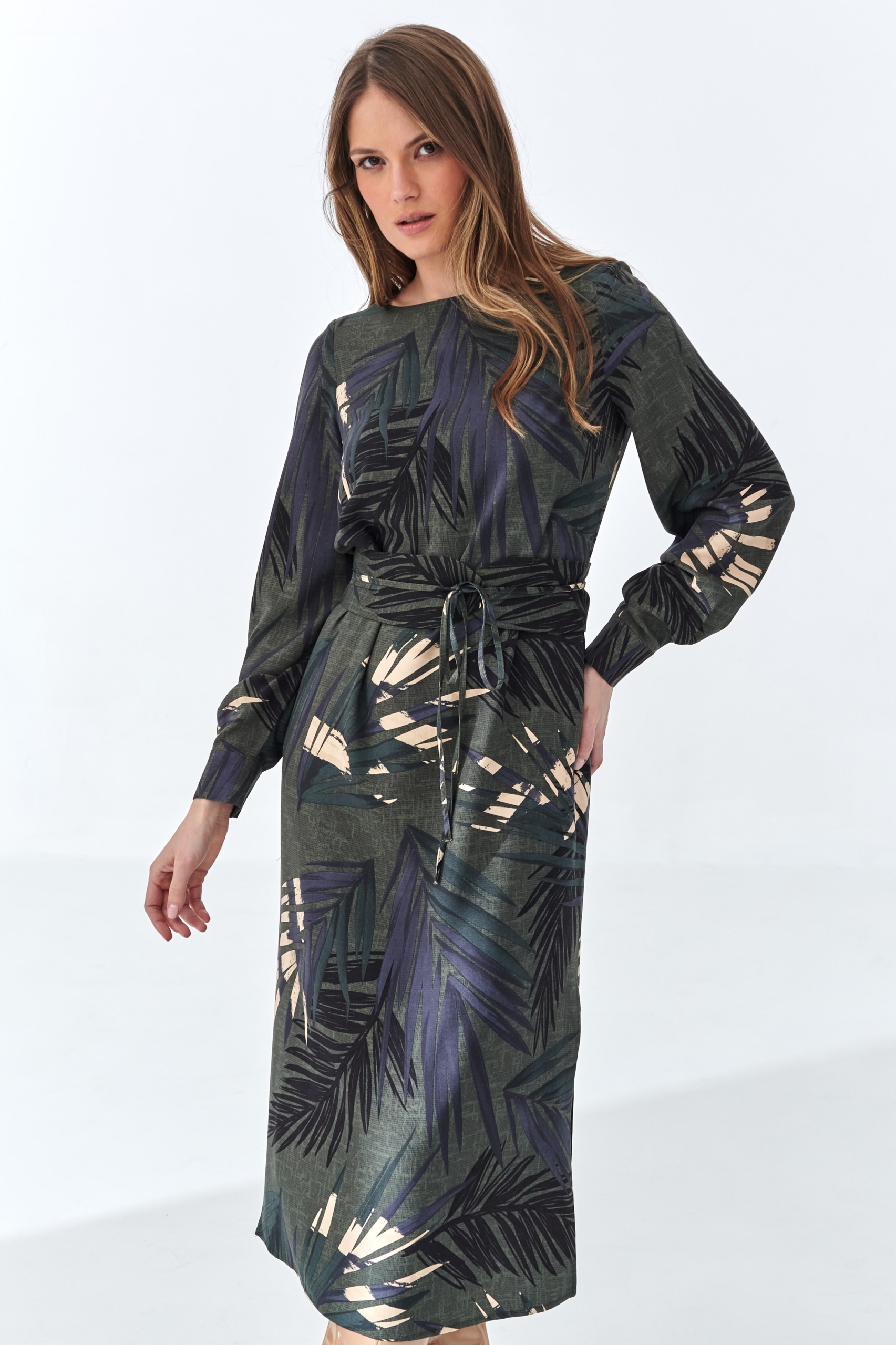 Modelka w ciemnozielonej sukience midi z wiskozy w palmowy print z paskiem w talii