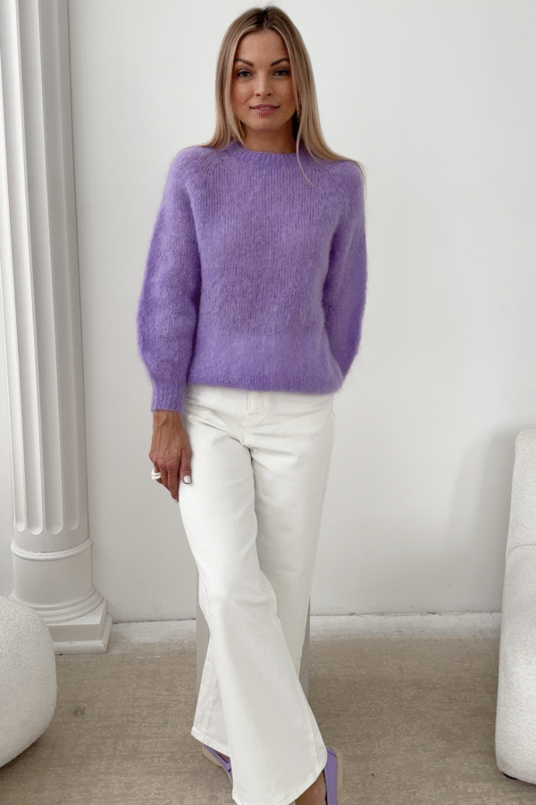 Kobieta w lawendowym swetrze z kid moheru i białych spodniach, ujęcie całości