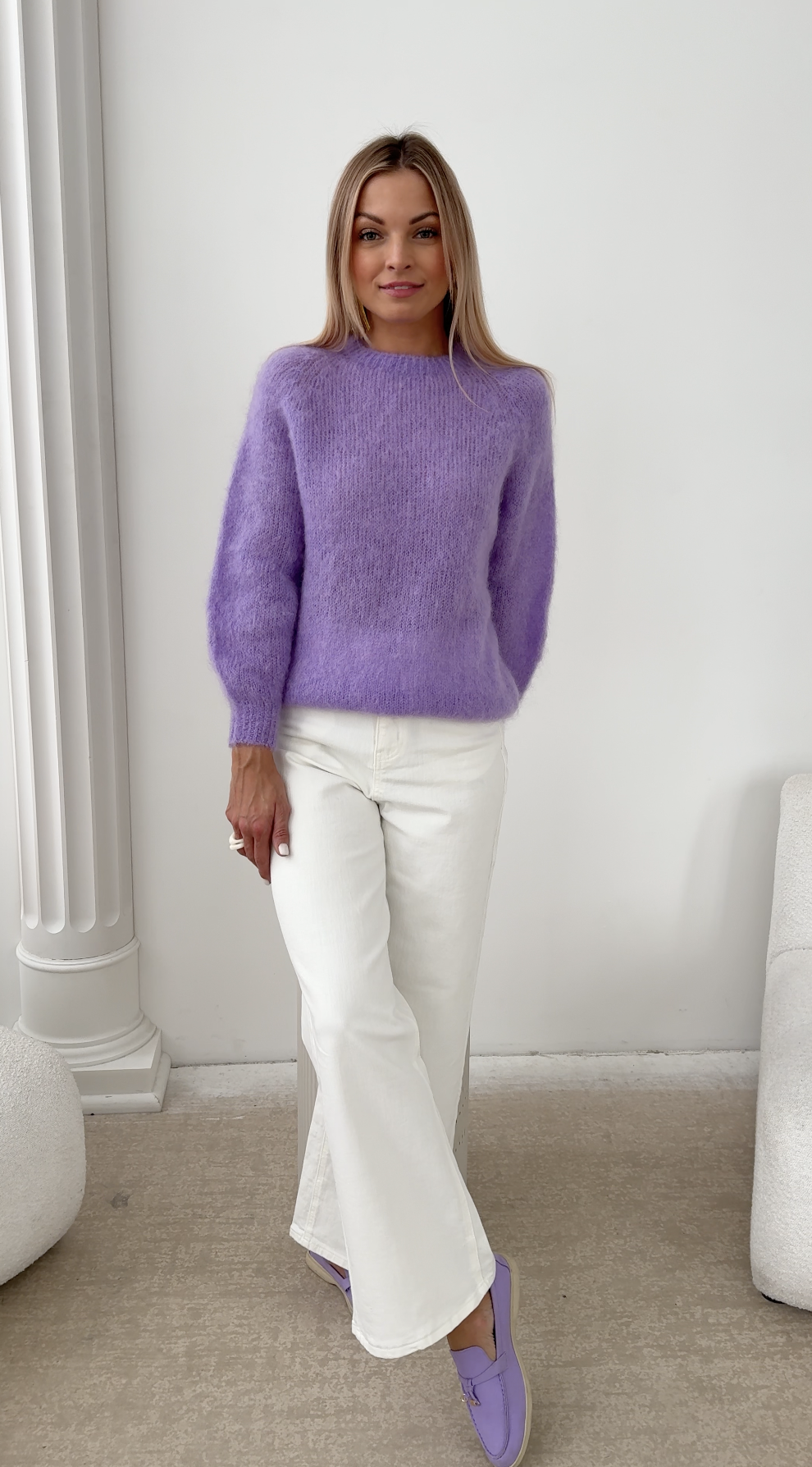 Kobieta w lawendowym swetrze z kid moheru i białych spodniach, ujęcie całości