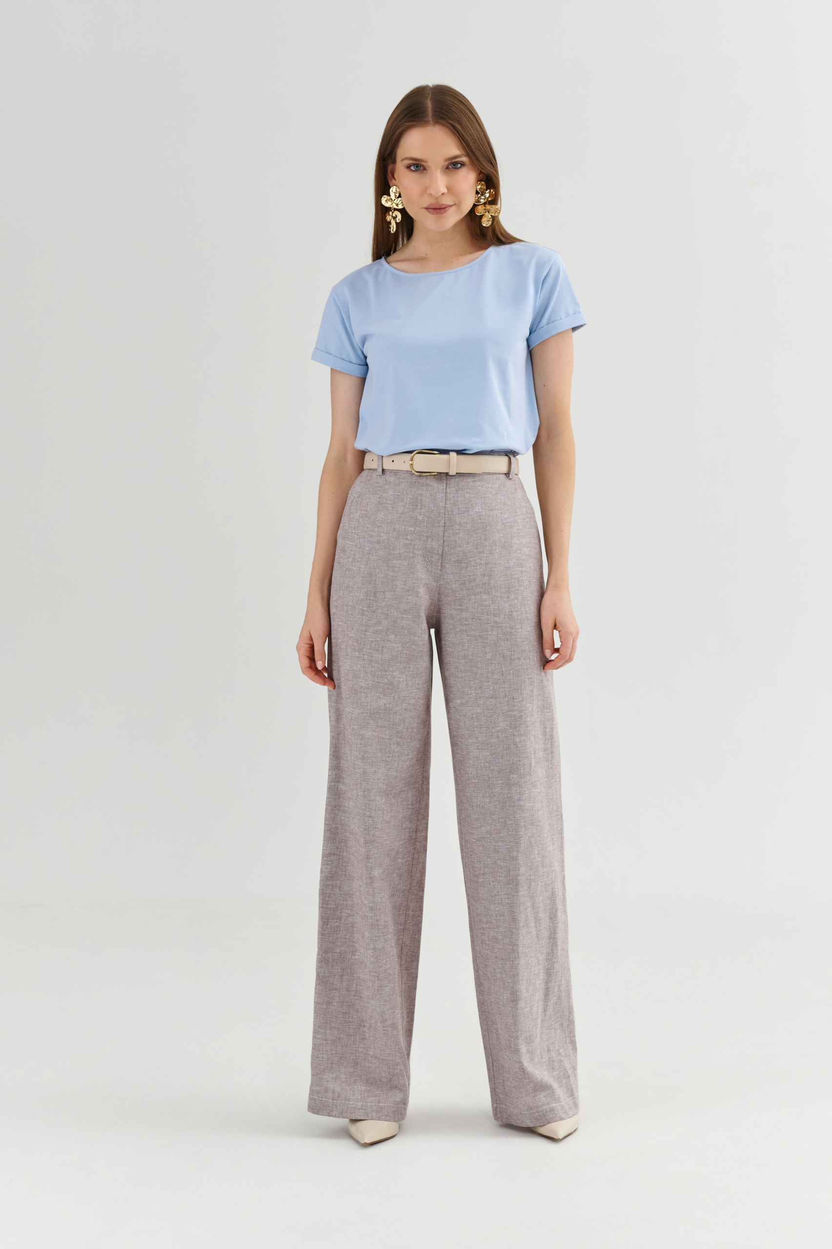 Modelka w błękitnym t-shircie basic z krótkim rękawem i jasnych szerokich spodniach z paskiem.