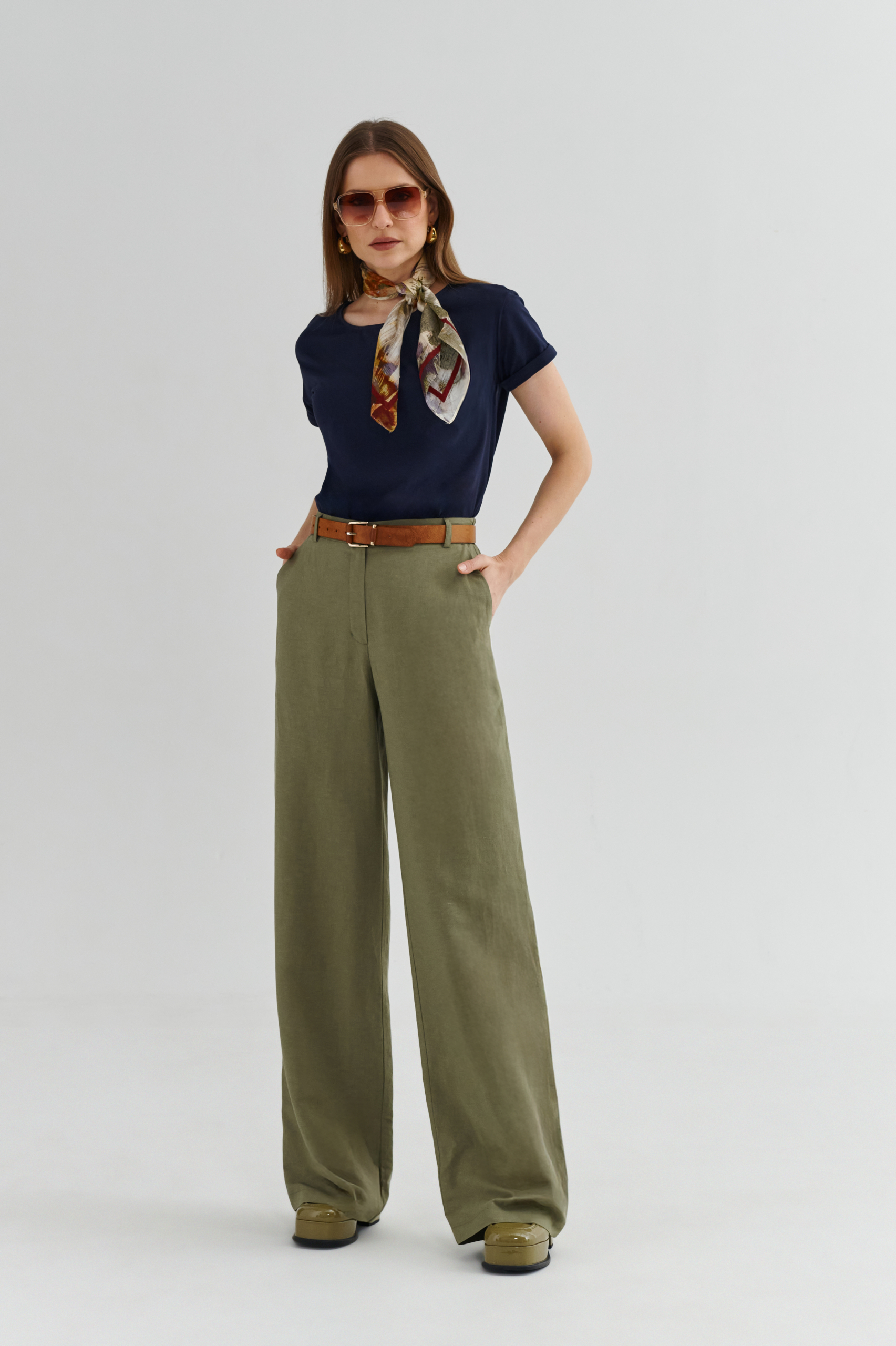 Zbliżenie: granatowy t-shirt damski pod oliwkową kurtką, apaszka przy szyi, pasek w kolorze koniaku.