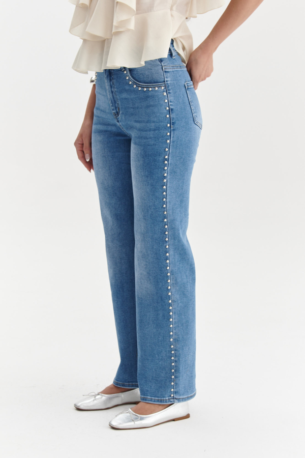 Zbliżenie na jasnoniebieskie jeansy z ozdobnymi srebrnymi nitami przy kieszeni i wzdłuż nogawki