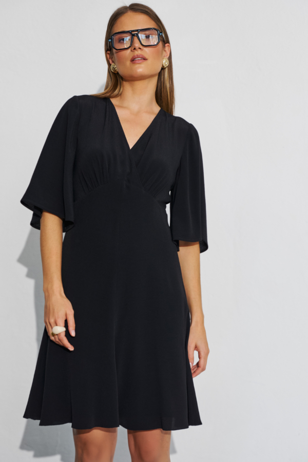 Modelka w czarnej krótkiej sukience rozkloszowanej z kopertowym dekoltem i szerokimi rękawami