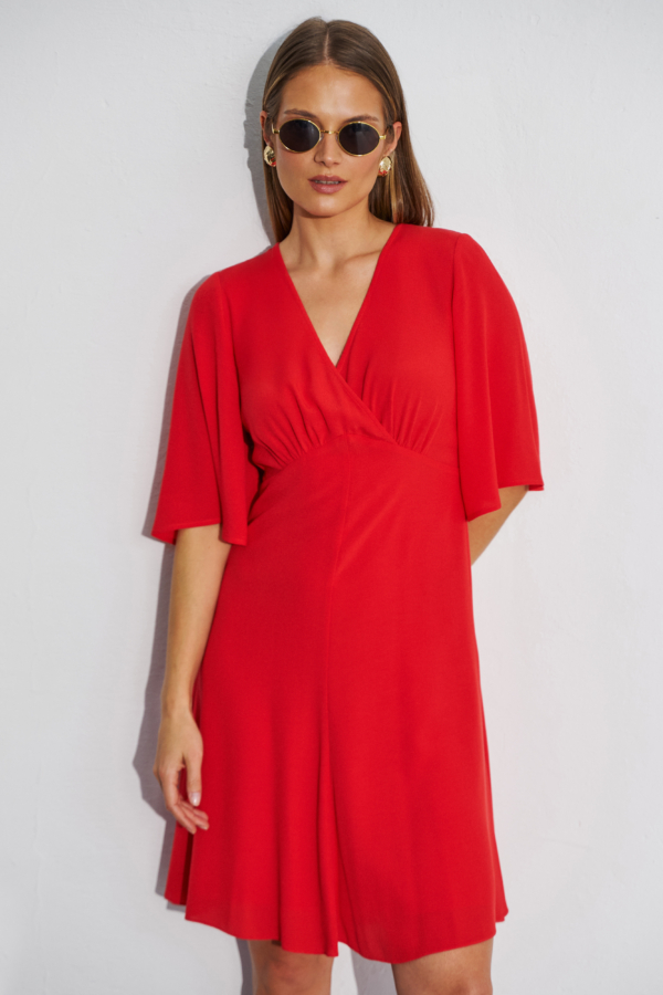 Modelka w czerwonej krótkiej sukience rozkloszowanej z kopertowym dekoltem i szerokimi rękawami