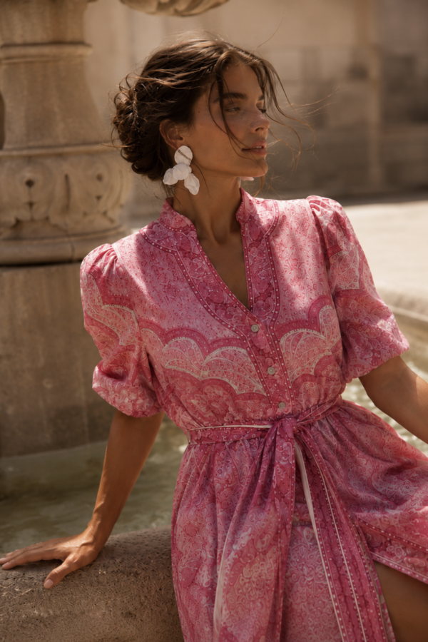 odelka w różowej sukience maxi w print paisley, z wiązaniem w talii, krótkim bufiastym rękawem i rozcięciem z przodu.
